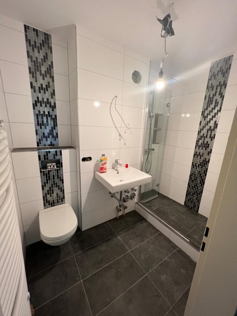 Badezimmer mit weißen Wandfliesen und senkrechter Mosaik-Bordüre an der Dusche