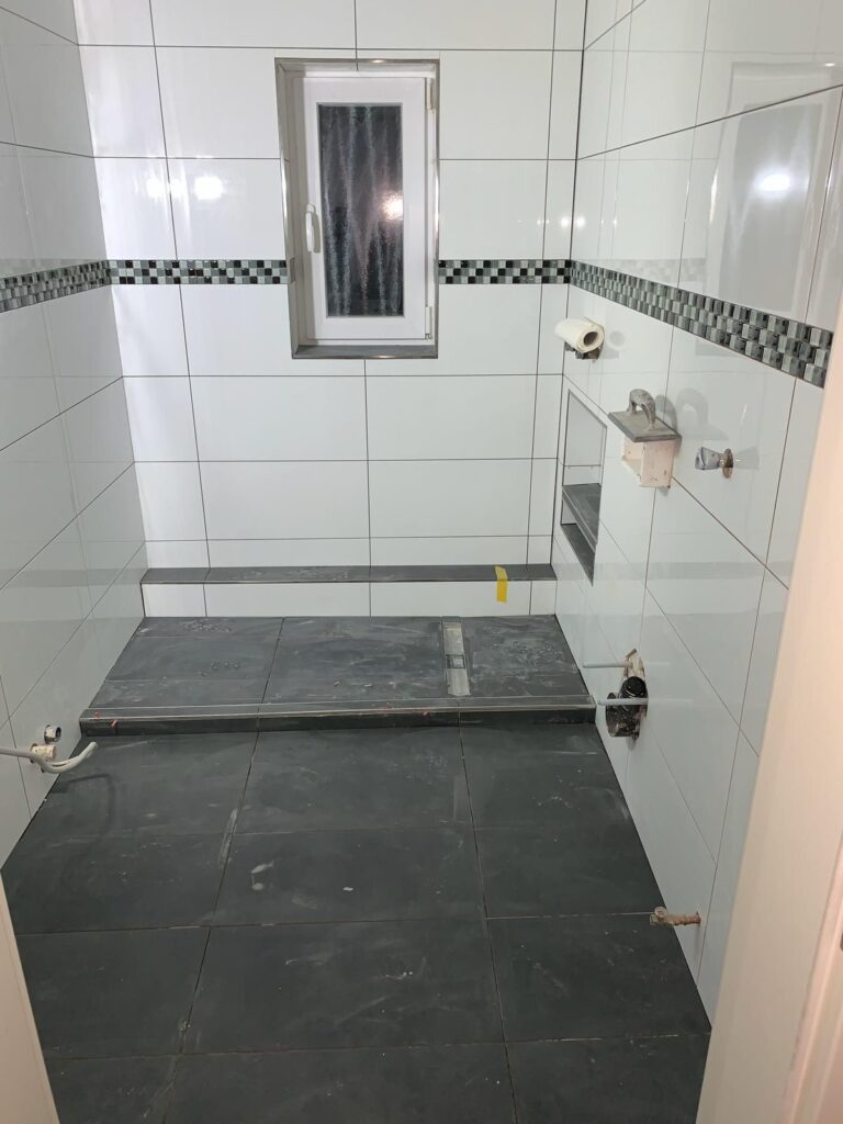 Bodengleiche Dusche mit weißen Wandfliesen und Glasabtrennung